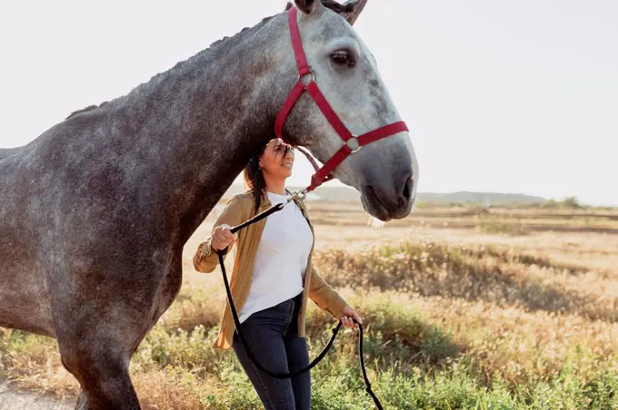 Woman holding horse bridle against meadow