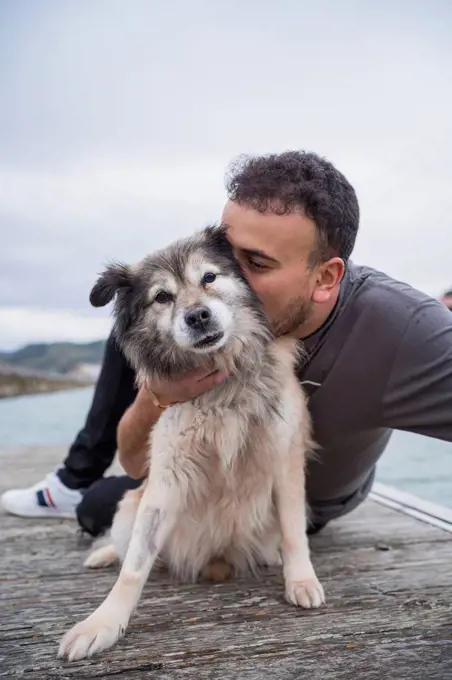 Man embracing dog while sitting on pier at beach against sky