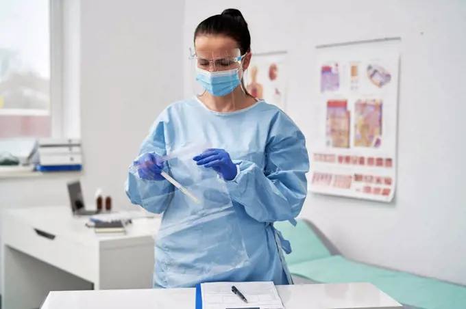 Mature female doctor with face shield putting medical sample in zipper bag