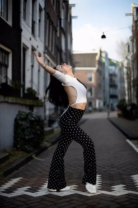 Woman dancing with arms outstretched on footpath at street