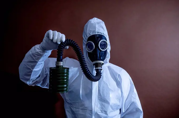 Mature in protective coveralls holding pipe of gas mask