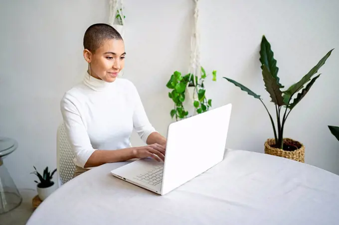 Smiling young female entrepreneur using laptop while working at home