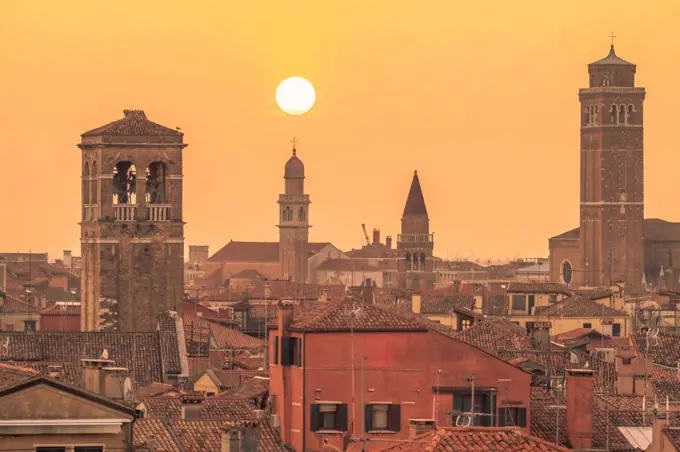 Italy, Veneto, Venice, Church bell towers rising over surrounding houses at moody sunset