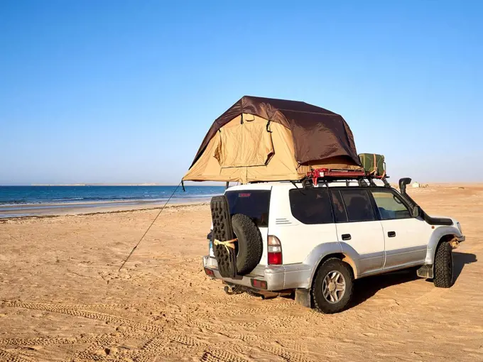 Tent pitched on top of roof of off-road vehicle parked on sandy coastal beach