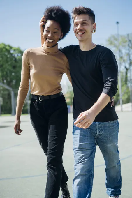 Cheerful couple walking at sports court during sunny day