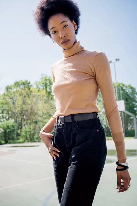 Young woman standing with hand in pocket at sports court during sunny day