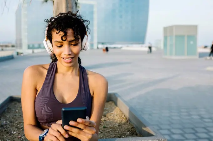 Female athlete with headphone using mobile phone in city