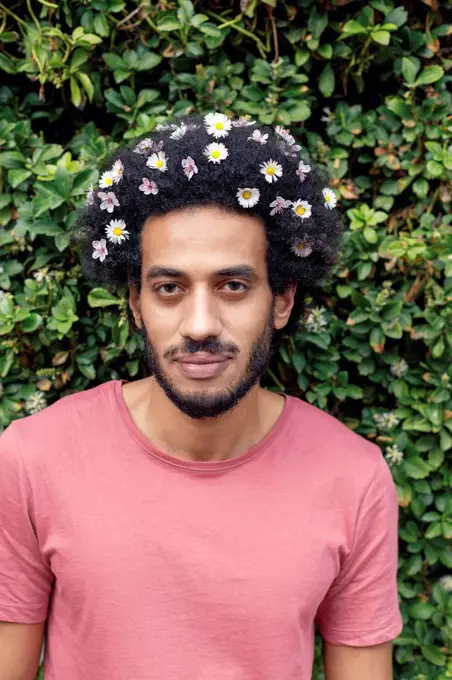 Afro young man with flowers in hair standing in front of plants