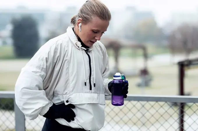 Exhausted female athlete drinking water after exercising in park