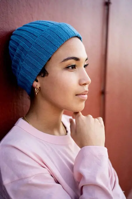 Beautiful woman with hand on chin day dreaming in front of wall