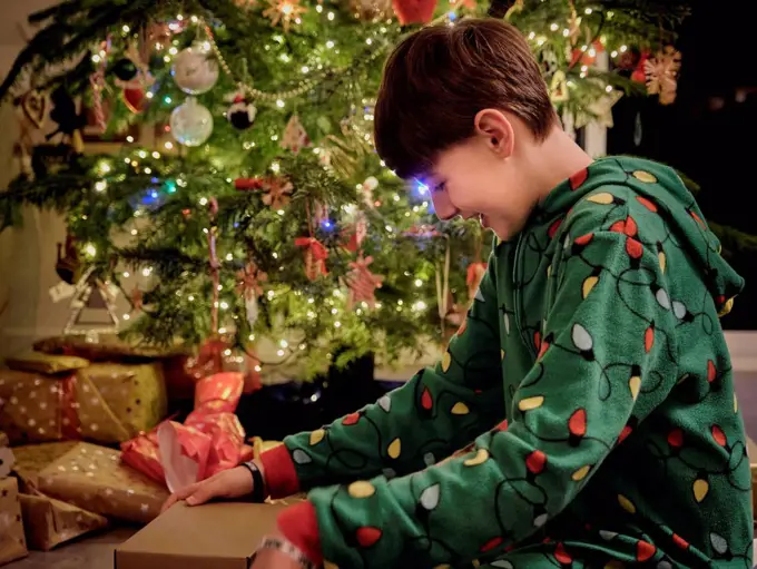 Smiling boy opening gift box by Christmas tree at home