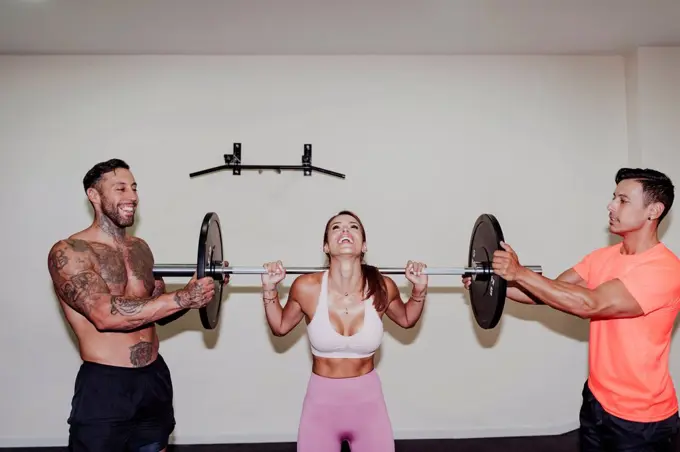 Male athletes helping female friend in exercising with barbell at gym