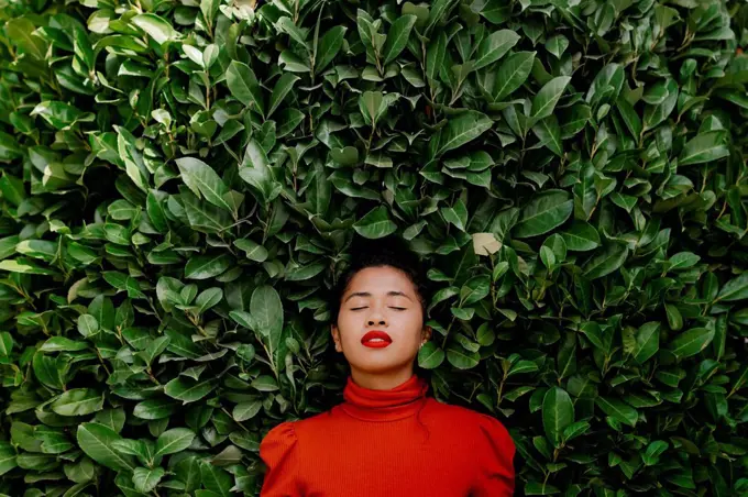 Woman with eyes closed in front of green plants