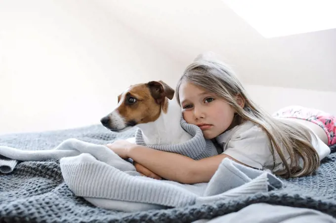 Cute girl embracing dog while lying on bed at home