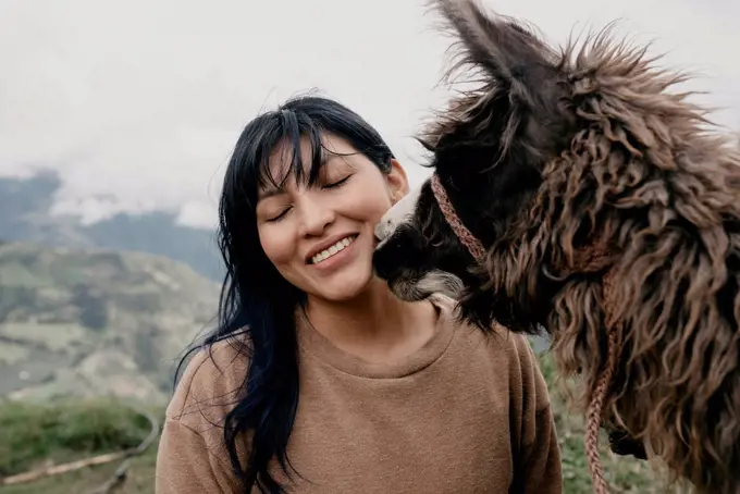 Smiling woman with eyes closed standing by Alpaca