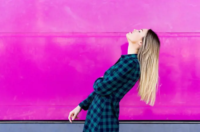 Young woman with head back standing by pink wall