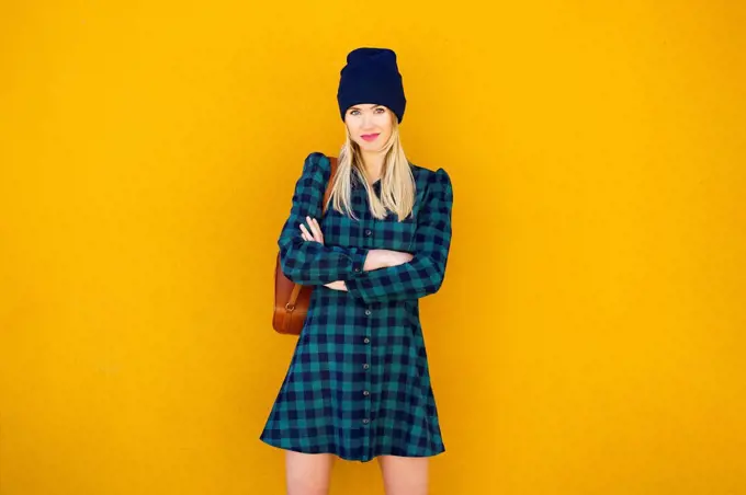 Beautiful woman with arms crossed standing in front of yellow wall