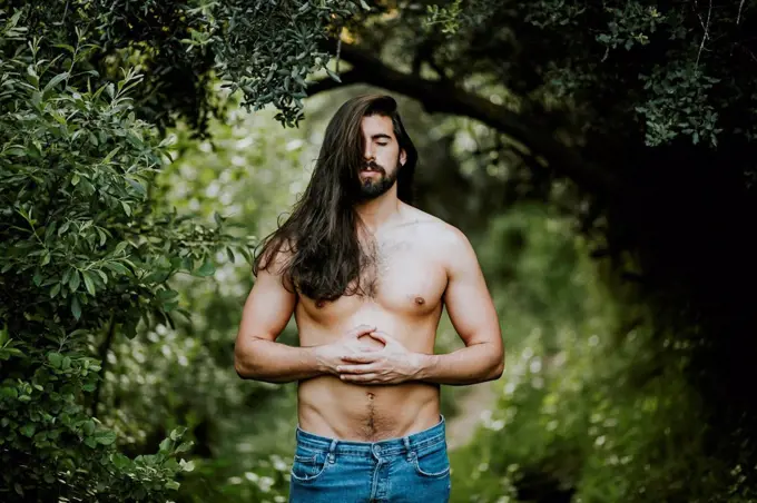 Shirtless man with eyes closed standing and relaxing in forest