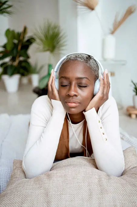 Beautiful woman with eyes closed listening music through headphones while lying at home