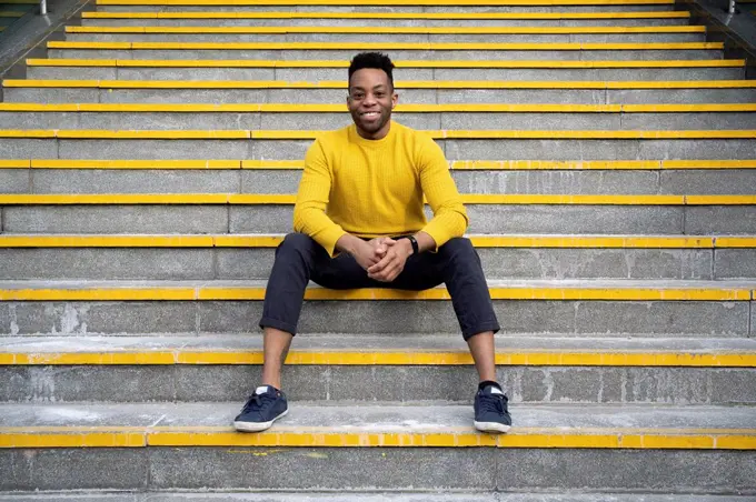 Smiling man with hands clasped sitting on staircase