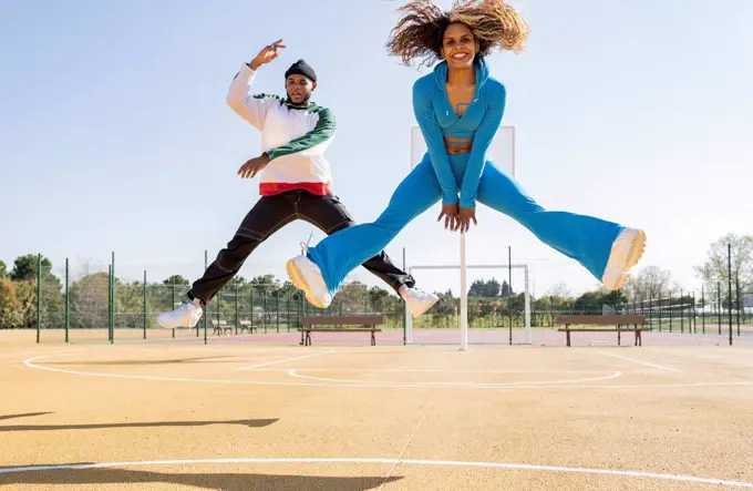 Confident male and female friends jumping while dancing on basketball court