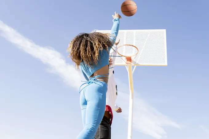 Female friend shooting in basketball hoop while playing on sports court