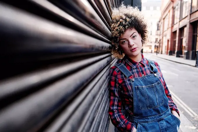 Hipster woman with hands in pockets leaning on shutter