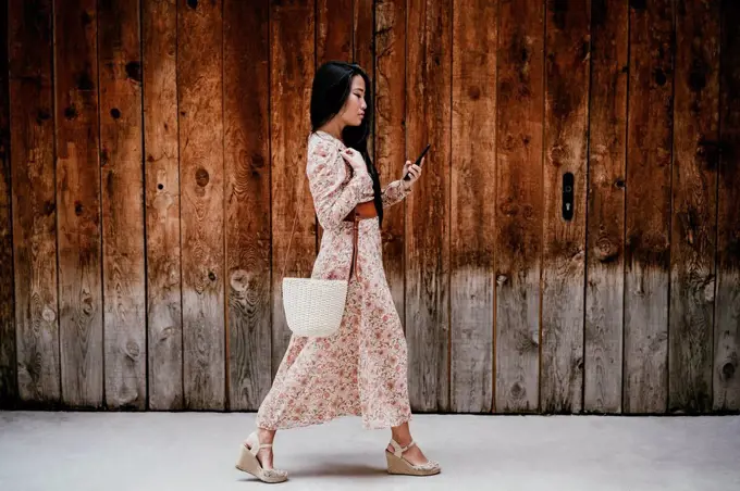 Woman using smart phone while walking by by old wooden door