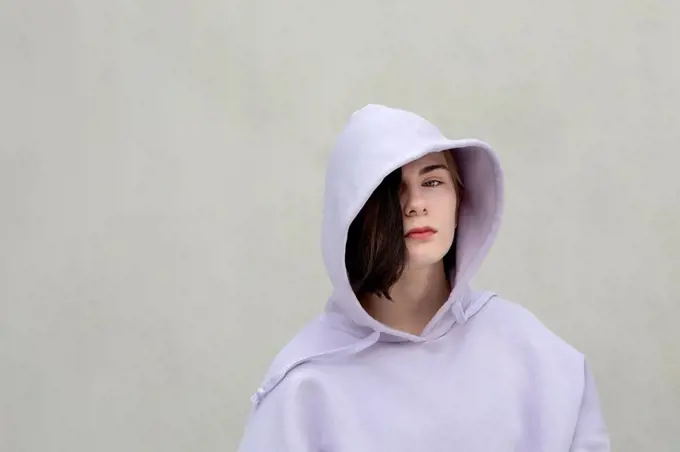 Beautiful teenage girl in hooded shirt by wall