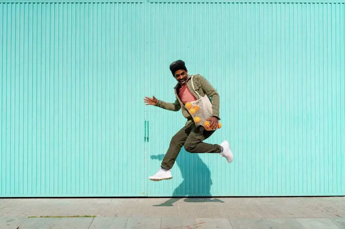 Ecstatic man dancing in front of turquoise wall during sunny day