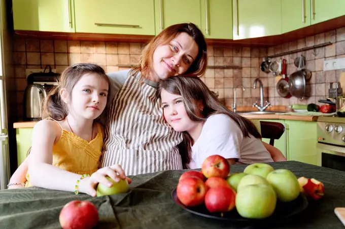 Smiling mother embracing daughters while sitting in kitchen at home