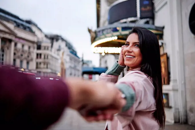 Happy young woman holding hand of boyfriend n city