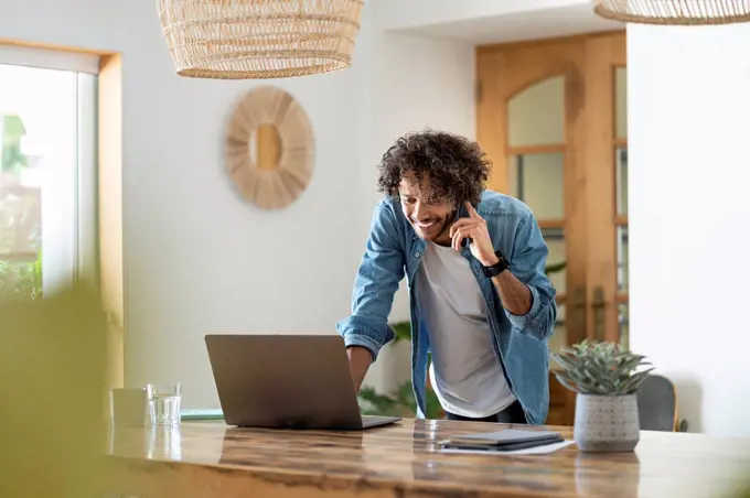 Male entrepreneur using laptop while talking on phone at home