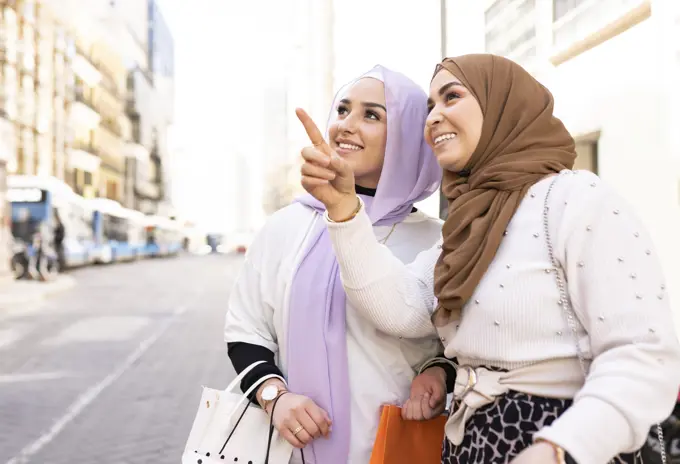 Young woman pointing to female friend while shopping in city