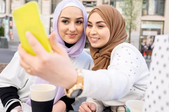 Young woman taking selfie through smart phone with female friend in city