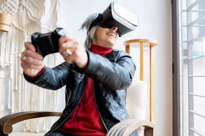 Smiling woman with game controller playing through virtual reality simulator at home