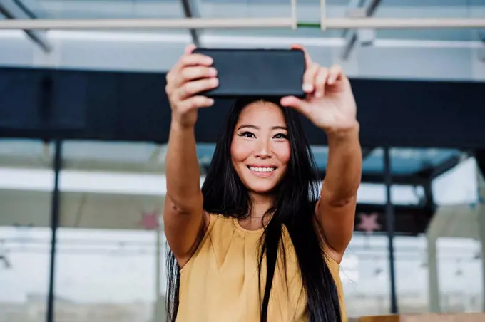 Happy businesswoman taking selfie from smart phone at office cafeteria