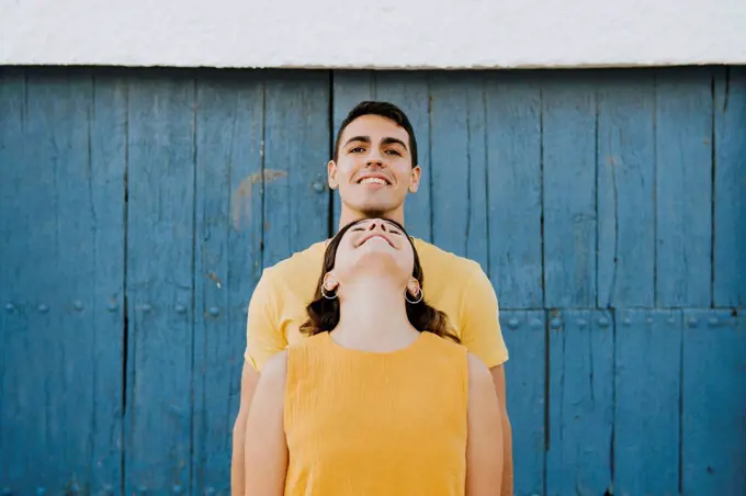 Young woman leaning on smiling man in front of wall