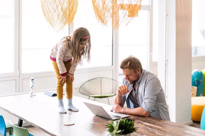 Businessman using laptop by daughter standing on table at home