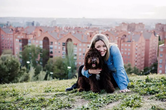 Happy woman embracing Spanish Water Dog in front of cityscape