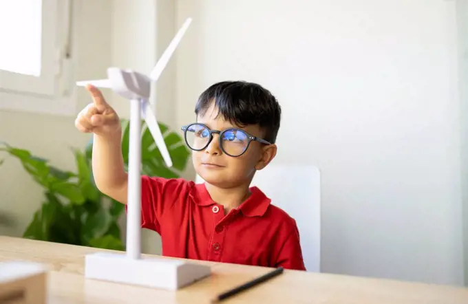 Boy wearing eyeglasses playing with wind turbine model at home
