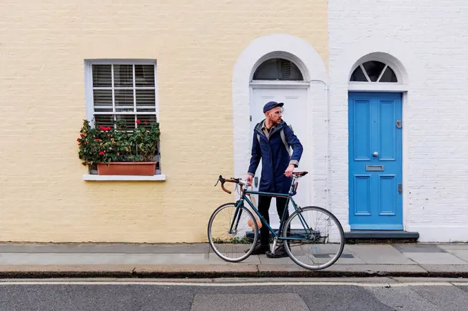 Young man looking away while holding bicycle on footpath