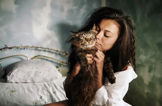 Woman embracing cat while sitting in bedroom