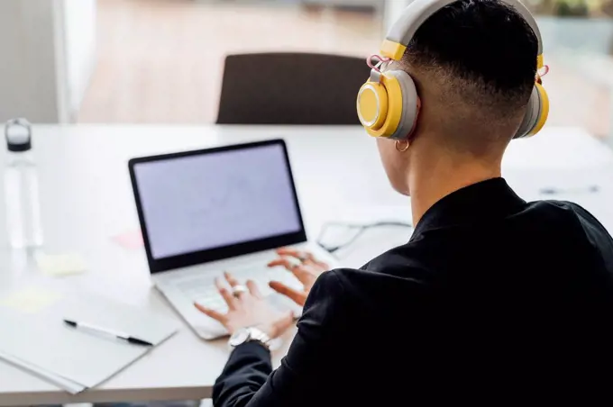 Female entrepreneur with headphones working on laptop in office