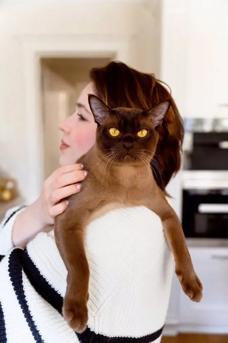 Female pet owner carrying Burmese cat on shoulder at home