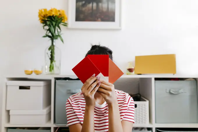 Young woman holding red color swatch in front of face at home