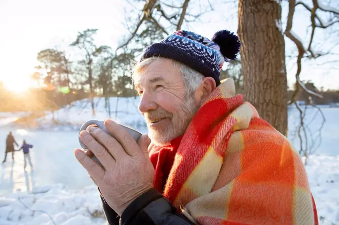 Senior man wrapped in blanket looking away while holding cup during winter