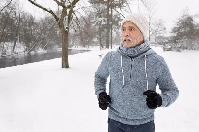 Senior man looking away while running at park during winter