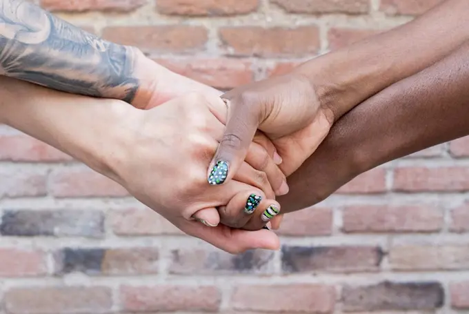 Multi-ethnic female friend holding hands in front of brick wall