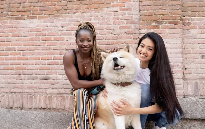 Multi-ethnic female friends with Akita Dog by brick wall